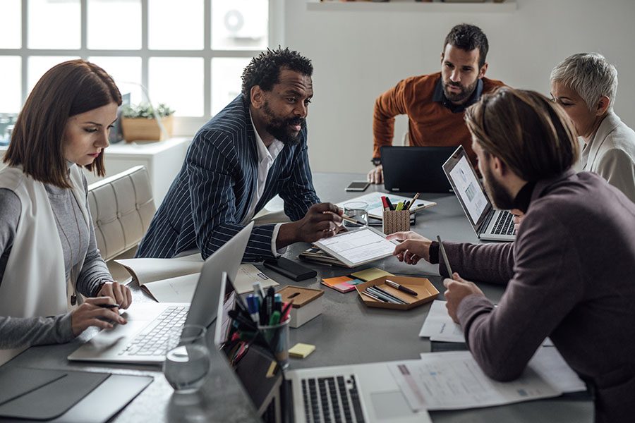 Business Insurance - Group of Diverse Employees Sitting Around a Table with Papers and Laptops During a Business Meeting in a Modern Office