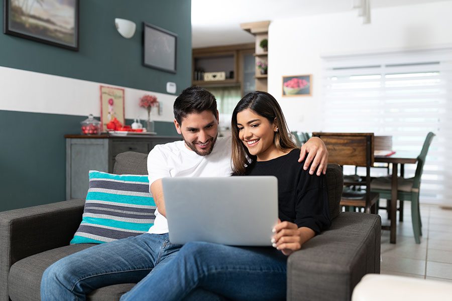 Hablamos Espanol - Portrait of a Cheerful Young Couple Sitting on a Sofa in the Living Room While Using a Laptop