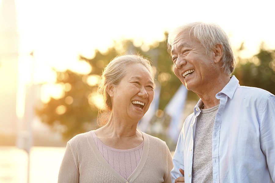 Medicare - Portrait of a Cheerful Smiling Elderly Couple Standing Outside in a Park on a Sunny Day at Sunset