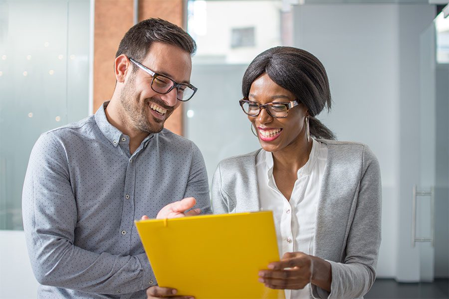 Self-Funded Employee Benefits - Portrait of a Cheerful Young Business Man and Woman Standing in the Office While Looking at Paperwork Together